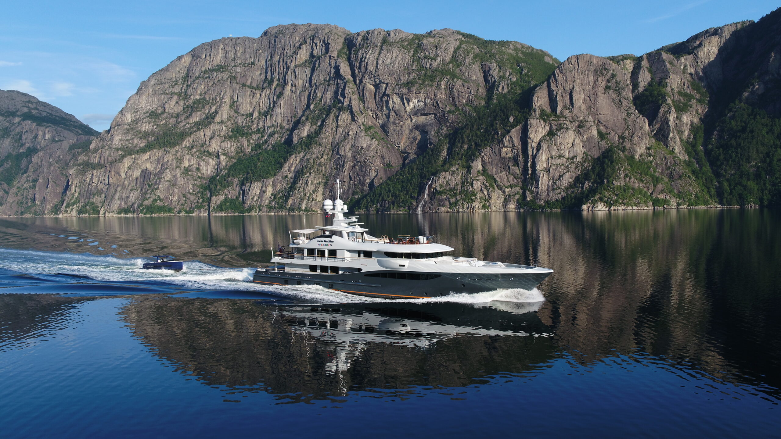 Superyacht under way in a fjord with tender alongside